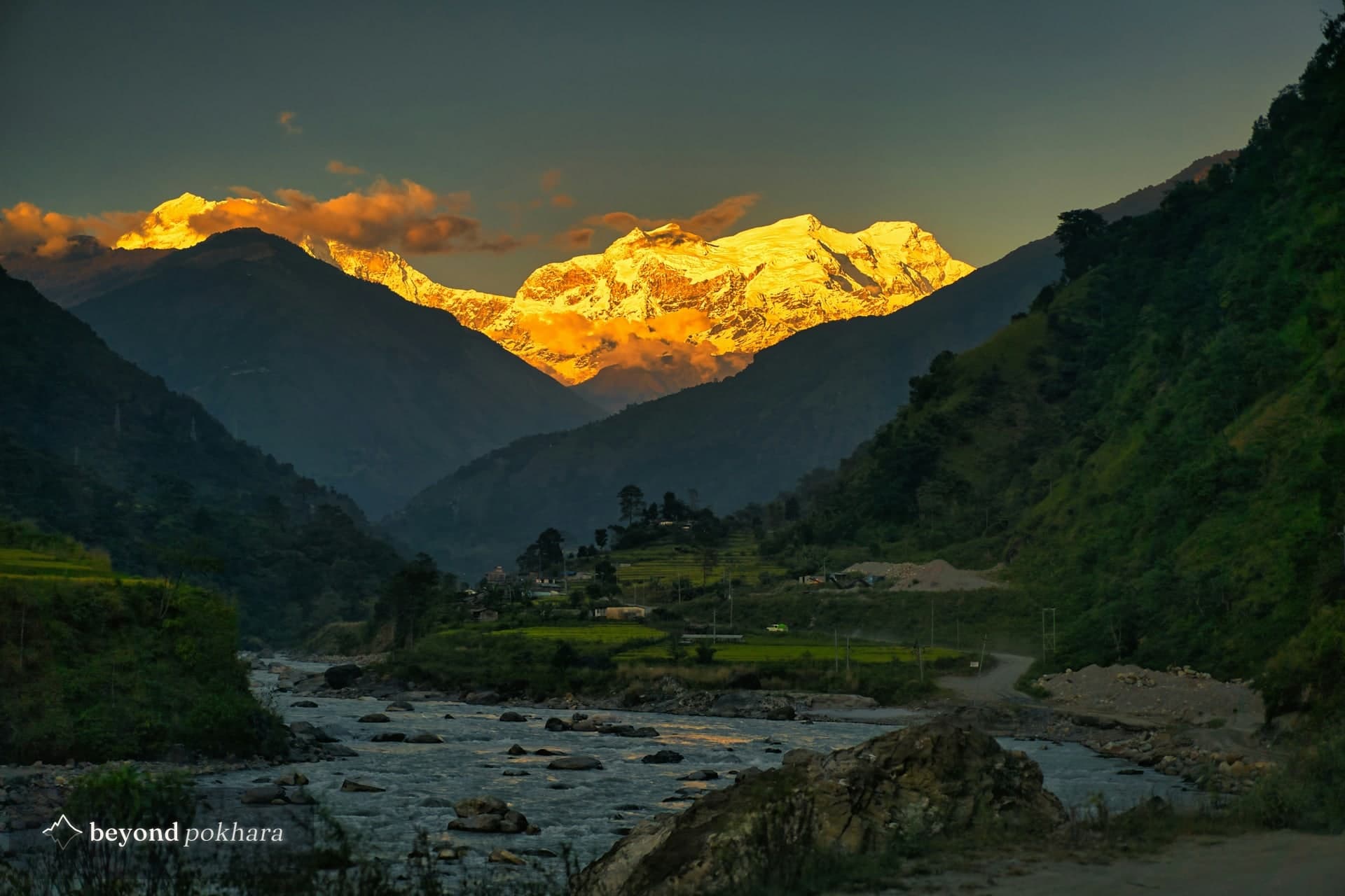 A village and road on the flat ground beside a braided Himalayan river below Annapurna, the valley geography behind the Nepal flash flood